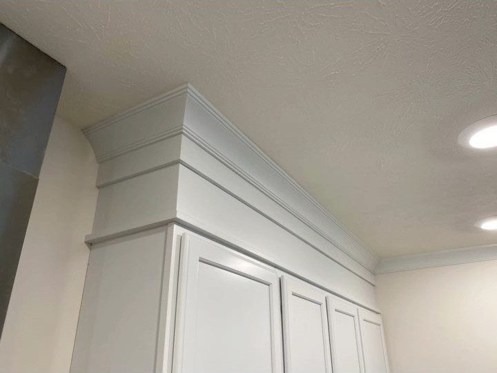 Adding Cabinets to Kitchen: 6 Ways to Gain Storage and Style 4 White kitchen cabinets with decorative crown molding installed against a white ceiling.
