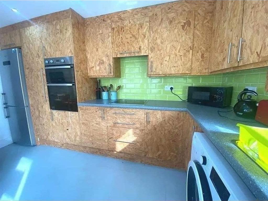 Adding Cabinets to Kitchen: 6 Ways to Gain Storage and Style 2 Kitchen cabinets constructed from textured oriented strand board with a green tiled backsplash and grey countertops.