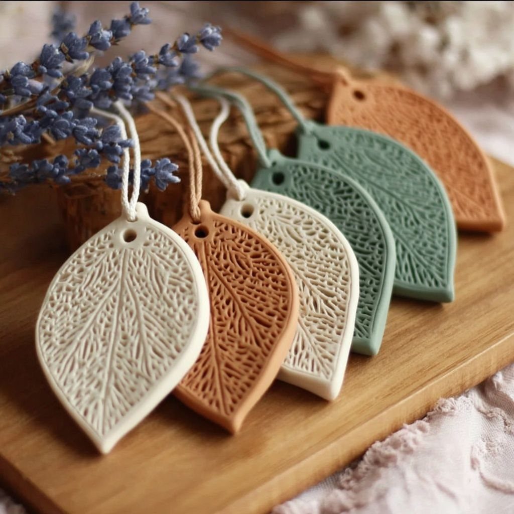 Leaf-shaped clay ornaments in various colors with small holes for hanging on a wooden surface.