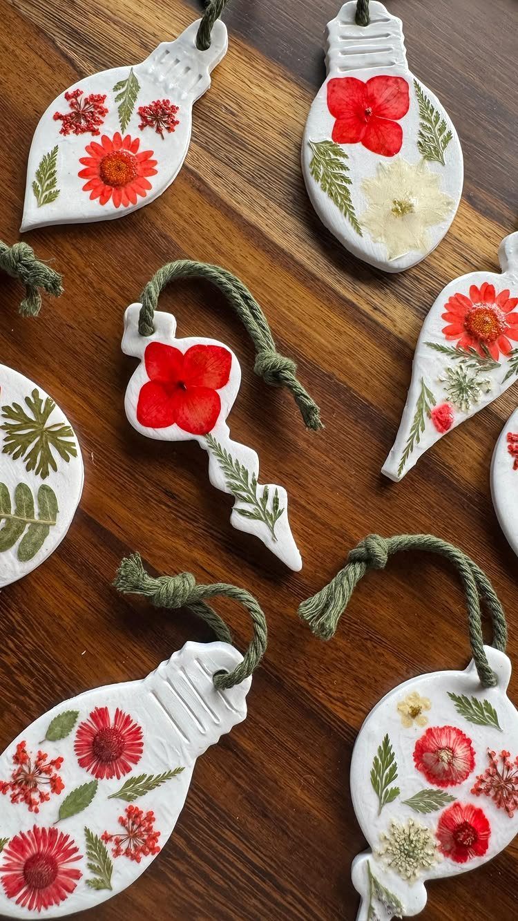 White clay lightbulb ornaments decorated with pressed red flowers and green leaves on wood.