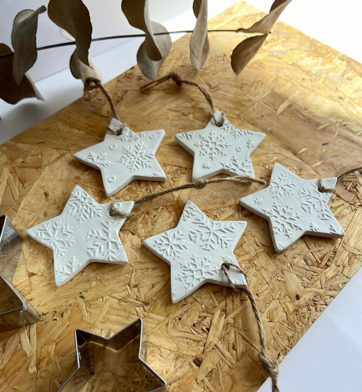 Five white star-shaped clay ornaments with snowflake impressions resting on a wooden surface with twine.