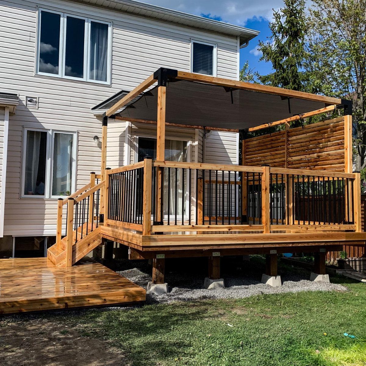 A wooden backyard deck featuring a large grey fabric awning for shade attached to a house.