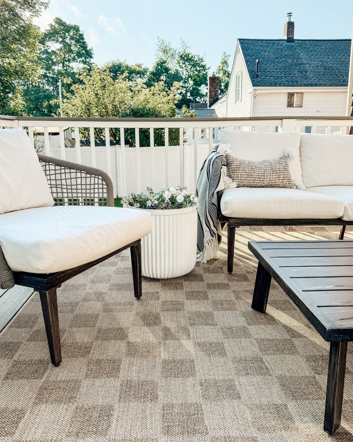 White outdoor lounge furniture sits on a checkered rug on a wooden deck.