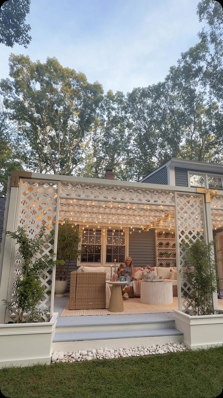 Wicker outdoor furniture with light cushions sits under string lights on a lattice-enclosed deck.