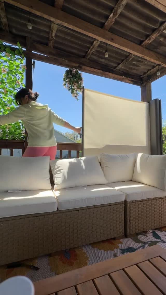 A person adjusting a large light-colored privacy screen on a wooden backyard deck.