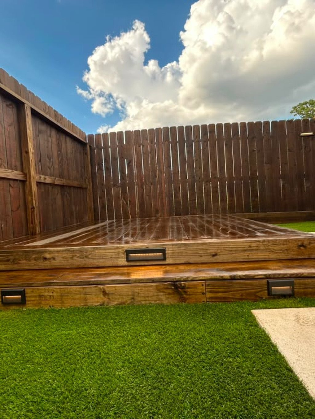 A wooden multi-level deck with small rectangular lights built into the steps near green grass.