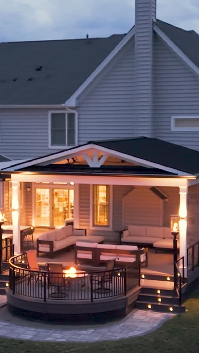 A circular wooden deck with built-in seating surrounding a glowing central fire pit at dusk.
