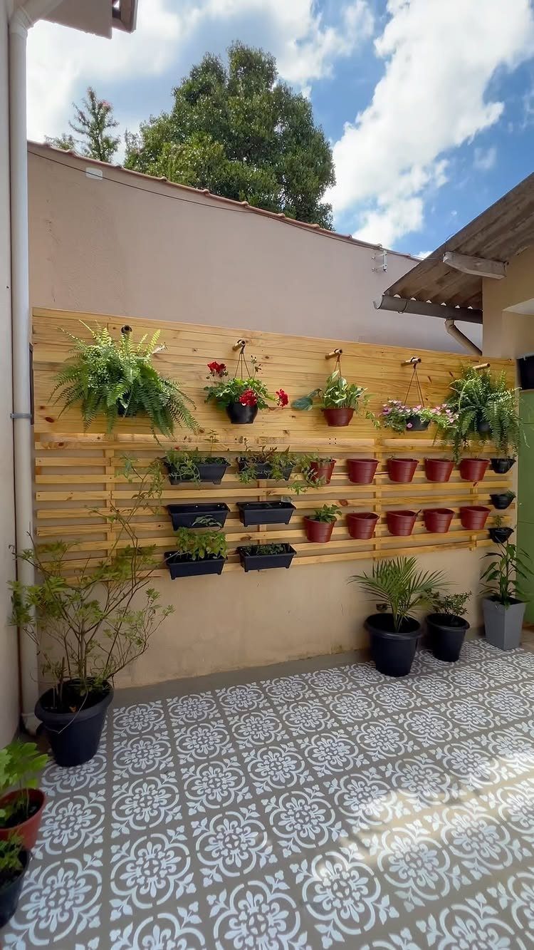 Wooden slat wall with various potted plants and flowers mounted on a beige exterior wall.