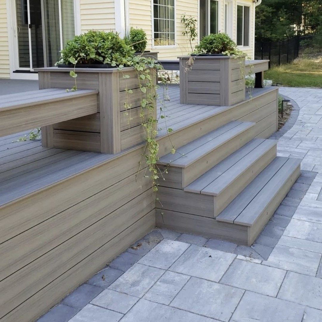 Grey composite deck with built-in wooden planters and integrated bench seating next to stone steps.