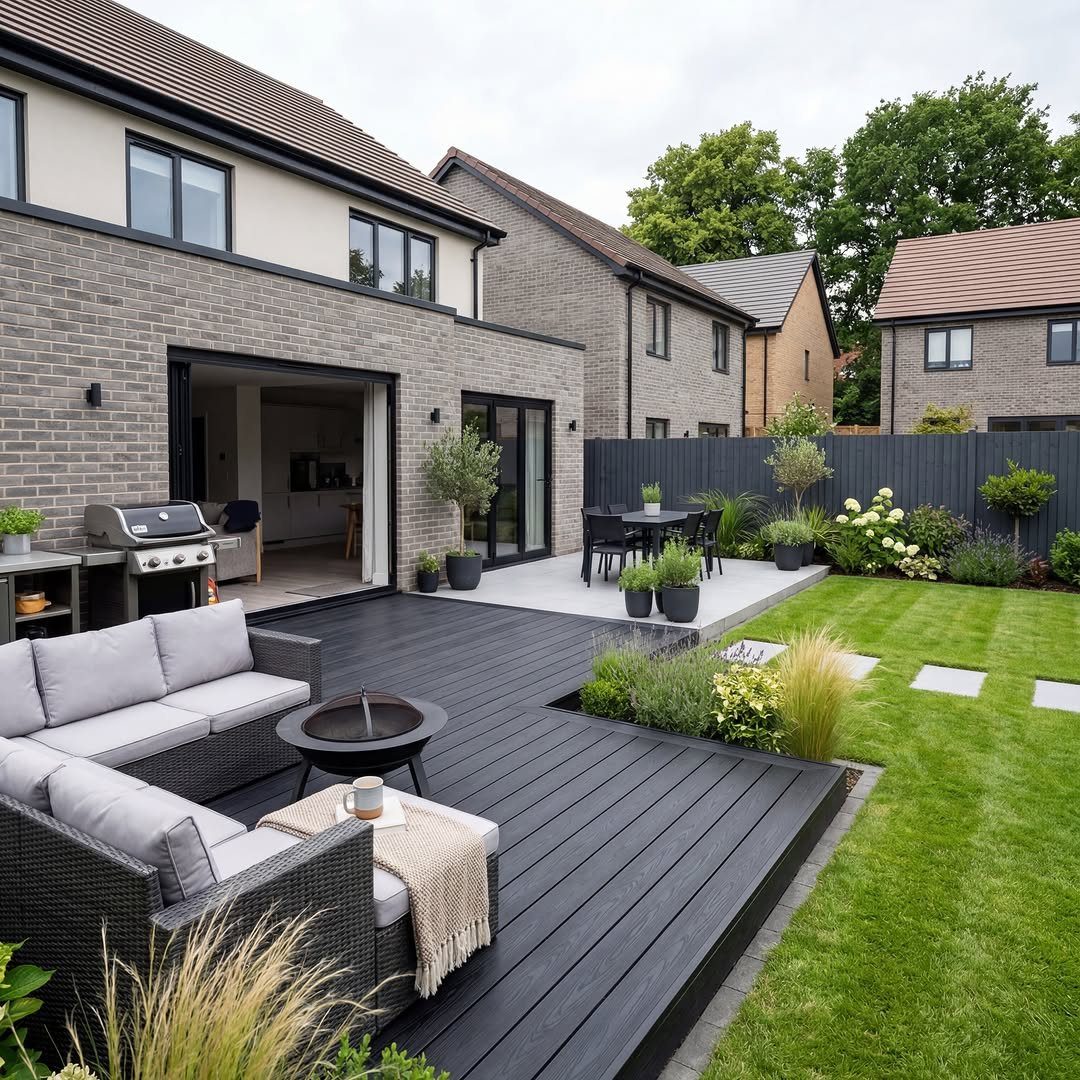 Dark grey composite decking surrounding a modern patio and green lawn next to a brick house.