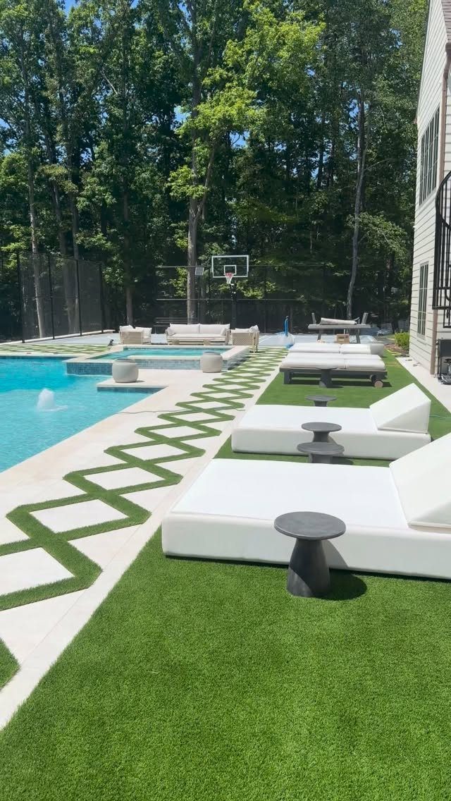 White lounge chairs and a swimming pool set against a backdrop of lush green trees.