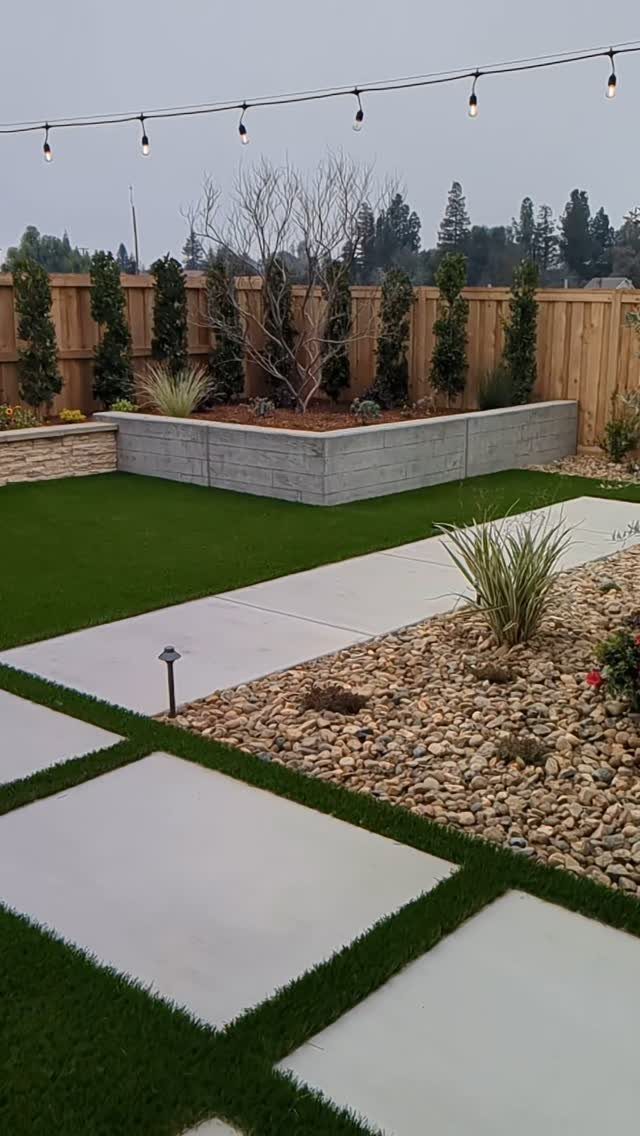 Large concrete pavers set in green turf next to a rock garden and retaining wall.