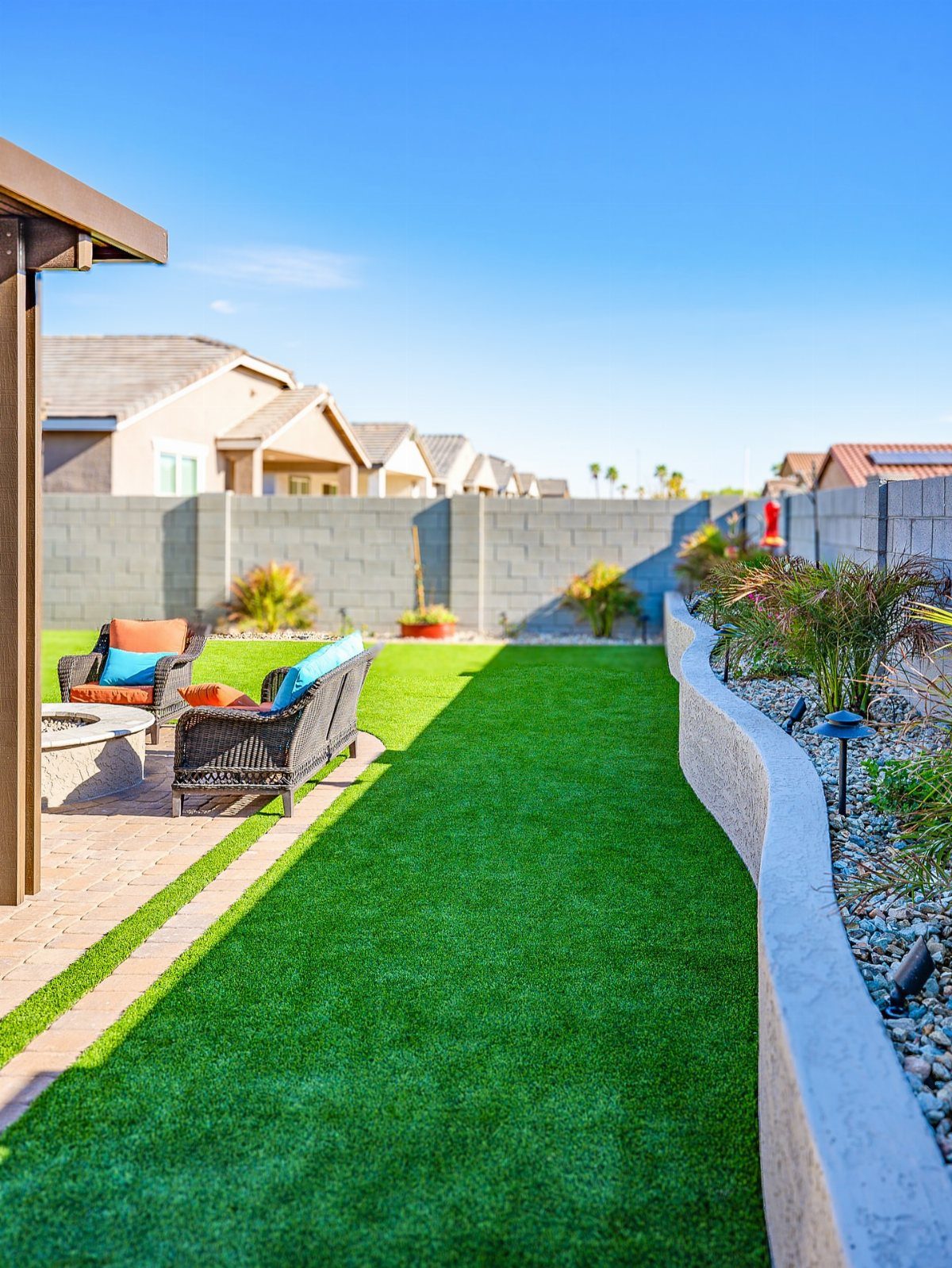 A manicured green lawn bordered by a curved concrete retaining wall and a stone patio.