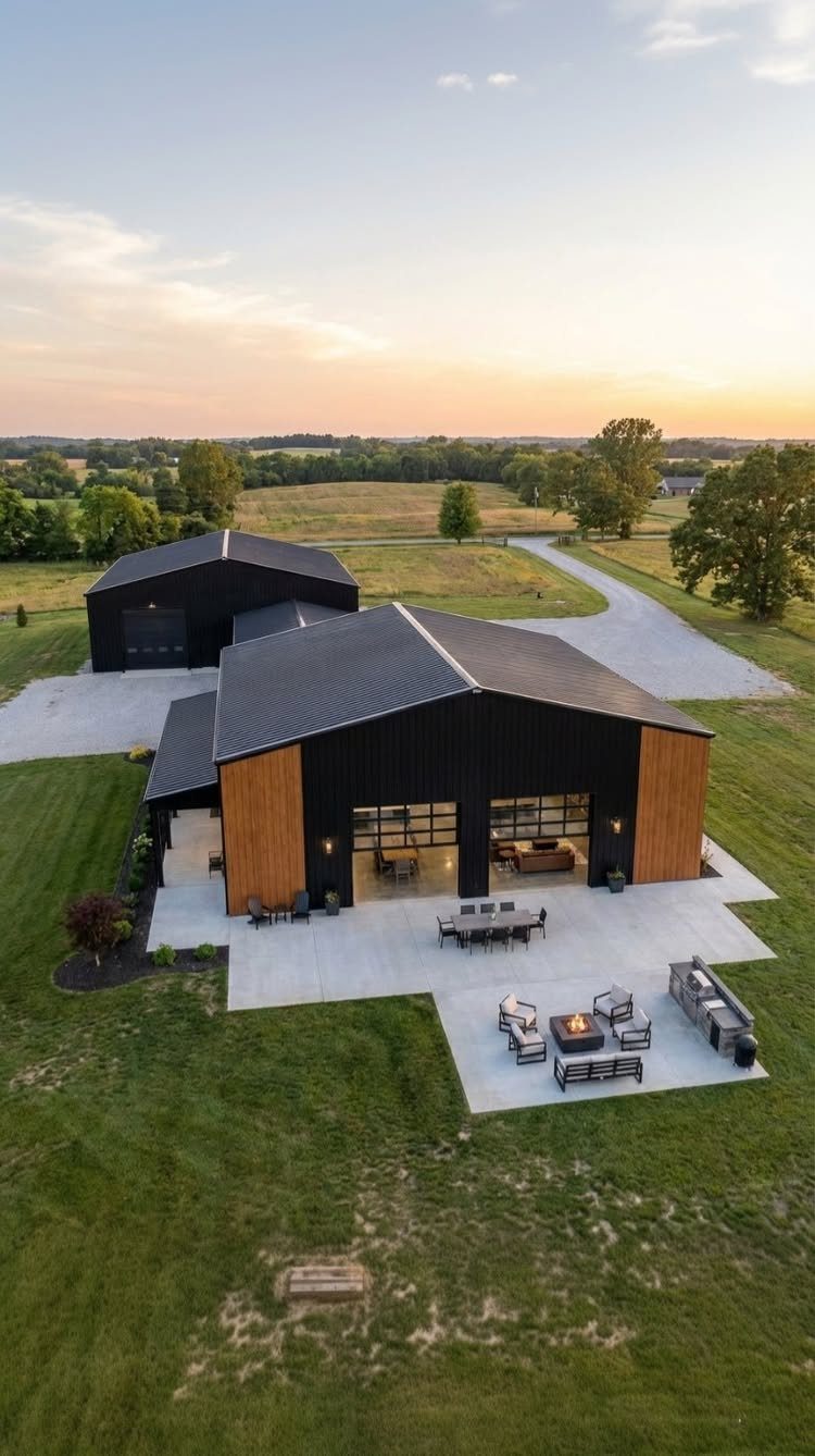 Barndominium Indoor Outdoor Kitchen: 8 Ideas That Erase the Wall 4 Aerial view of a modern black barndominium with wood siding and a large outdoor concrete patio.