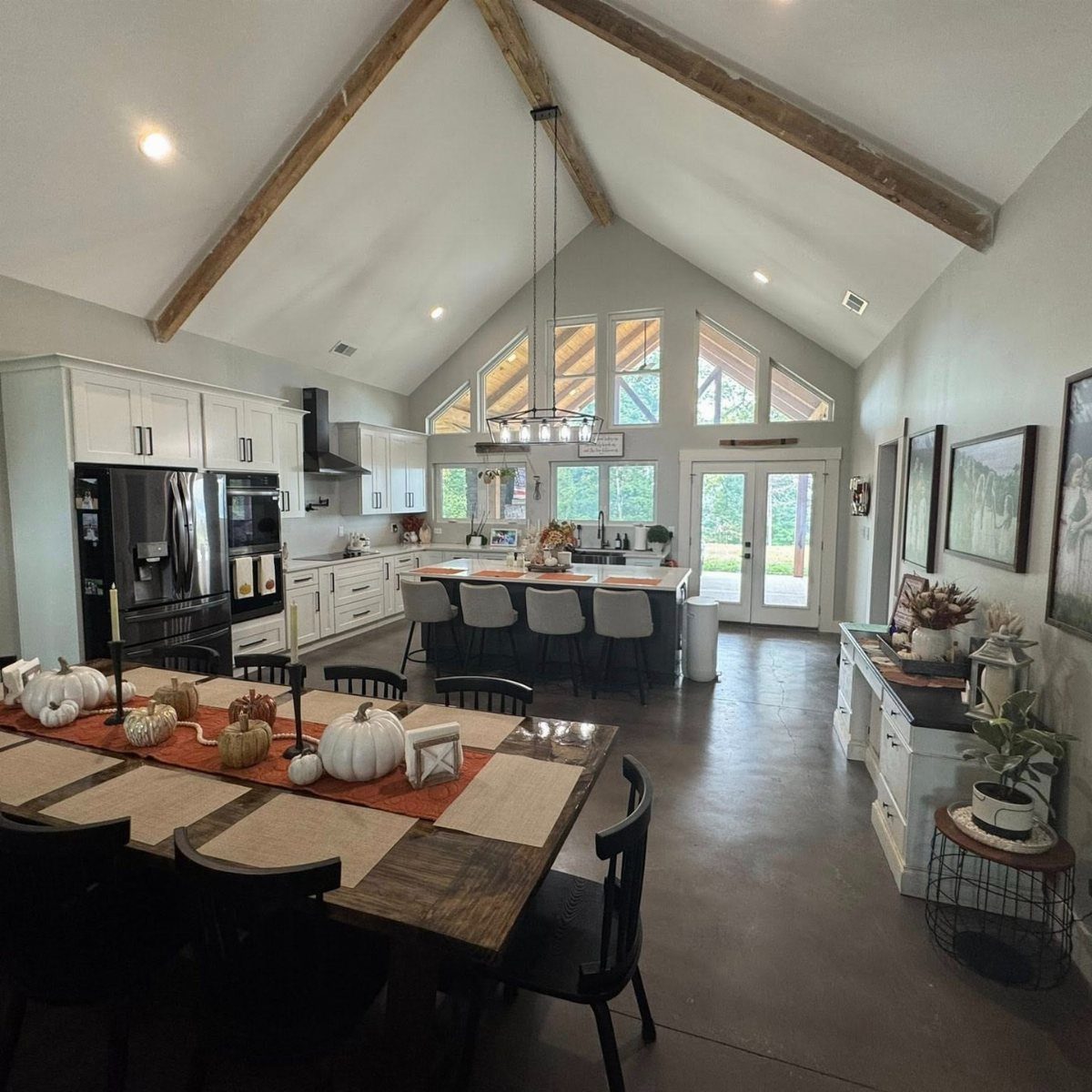 Barndominium Indoor Outdoor Kitchen: 8 Ideas That Erase the Wall 8 Spacious open-concept kitchen with vaulted ceilings, wooden beams, and large windows overlooking a green landscape.