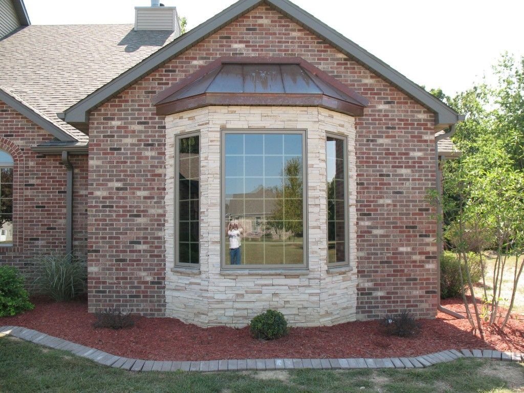 A bay window on a brick house featuring a light stone surround and red mulch landscaping.