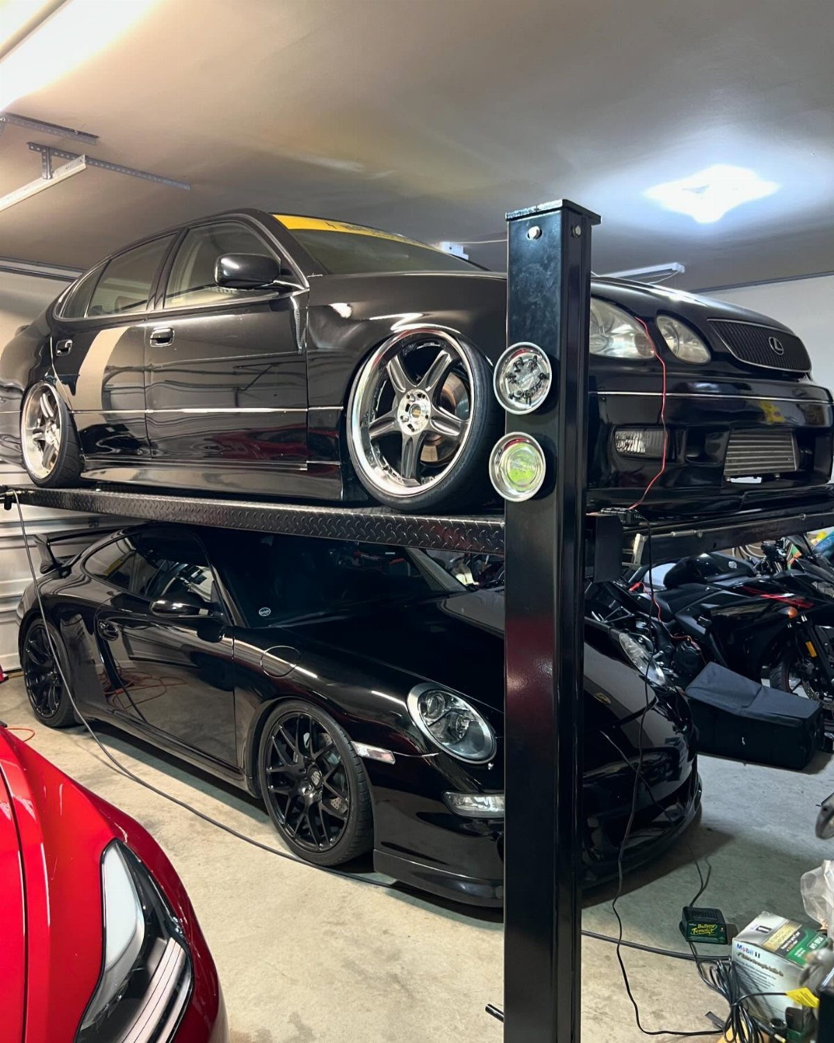 Two black cars parked in a garage with one car elevated on a metal vehicle lift.