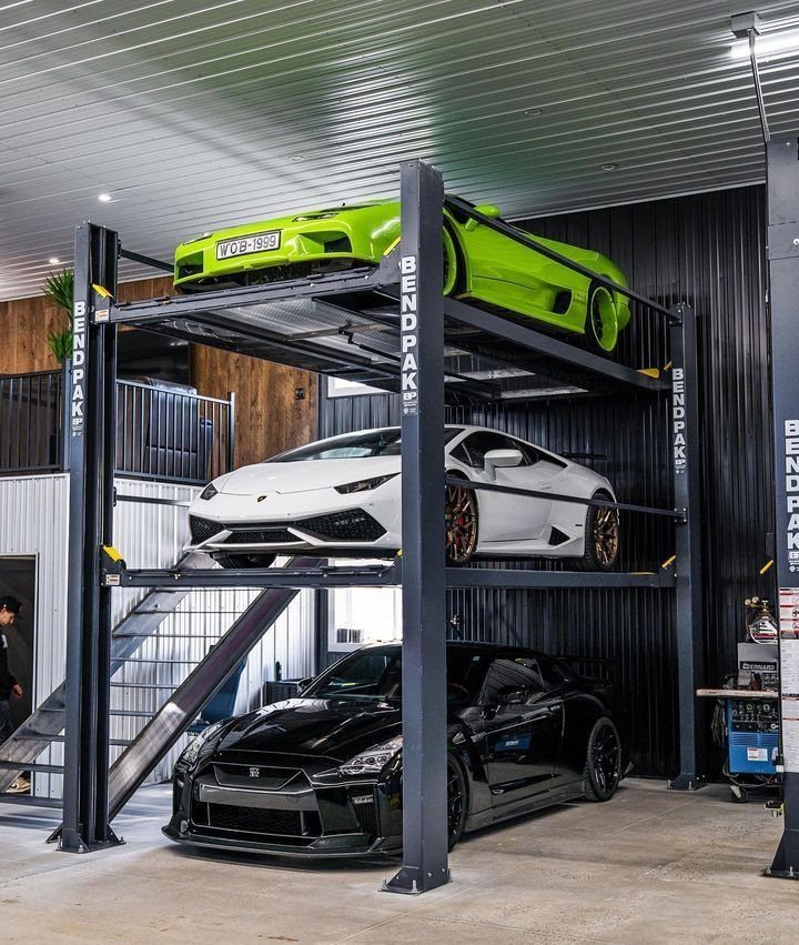 Three luxury sports cars stacked vertically on a black metal lift system in a modern garage.