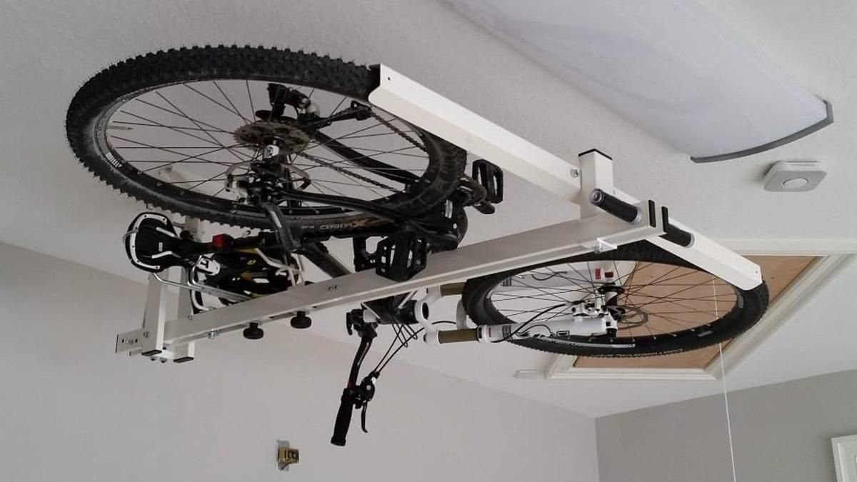 Two bicycles suspended from a white mechanical ceiling-mounted lift system indoors.