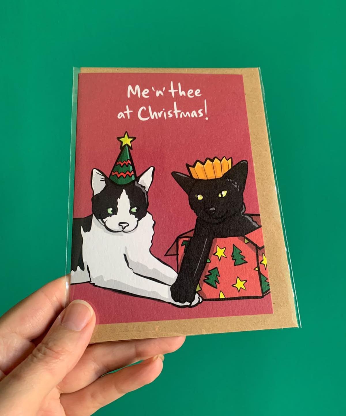 Black Cat Christmas: 8 Photo Ideas for the Holidays 4 A hand holding a Christmas card featuring two illustrated cats in a festive setting.