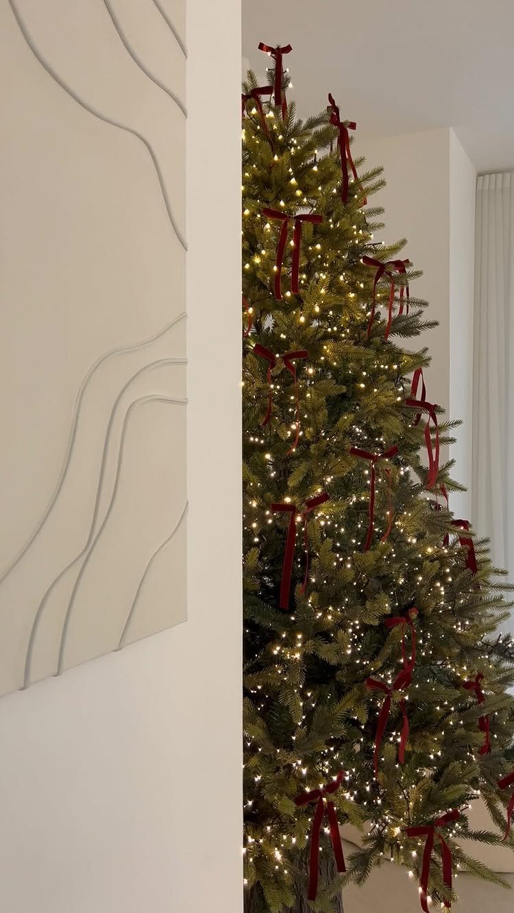 Burgundy Tree Decor: 9 Ideas Borrowed from High-End Design 5 A Christmas tree decorated with warm lights and burgundy velvet bows on green branches.