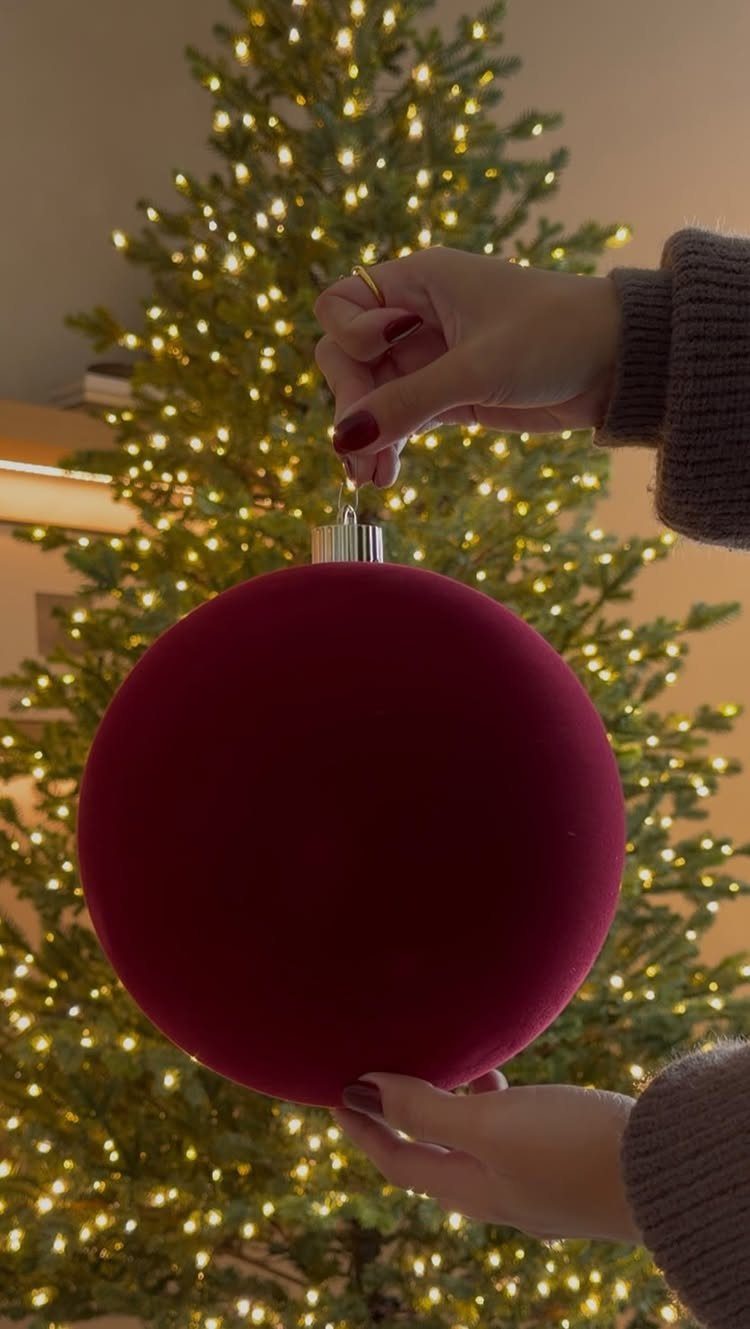 Burgundy Tree Decor: 9 Ideas Borrowed from High-End Design 3 Hands holding a large burgundy velvet Christmas ornament in front of a glowing Christmas tree.