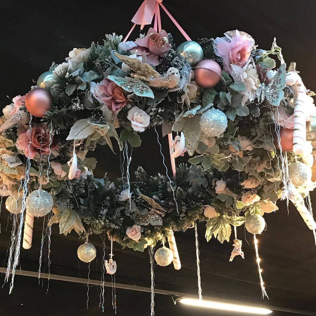 9 Ceiling Christmas Decor Ideas for 2026 4 A large festive wreath decorated with pink roses, silver ornaments, and hanging white strands suspended from a ceiling.