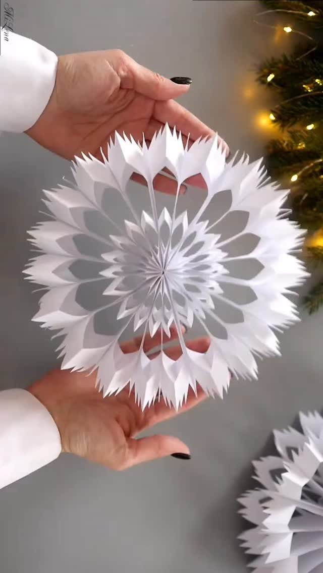 9 Ceiling Christmas Decor Ideas for 2026 6 Hands holding a large, intricate white paper snowflake decoration against a blurred background.