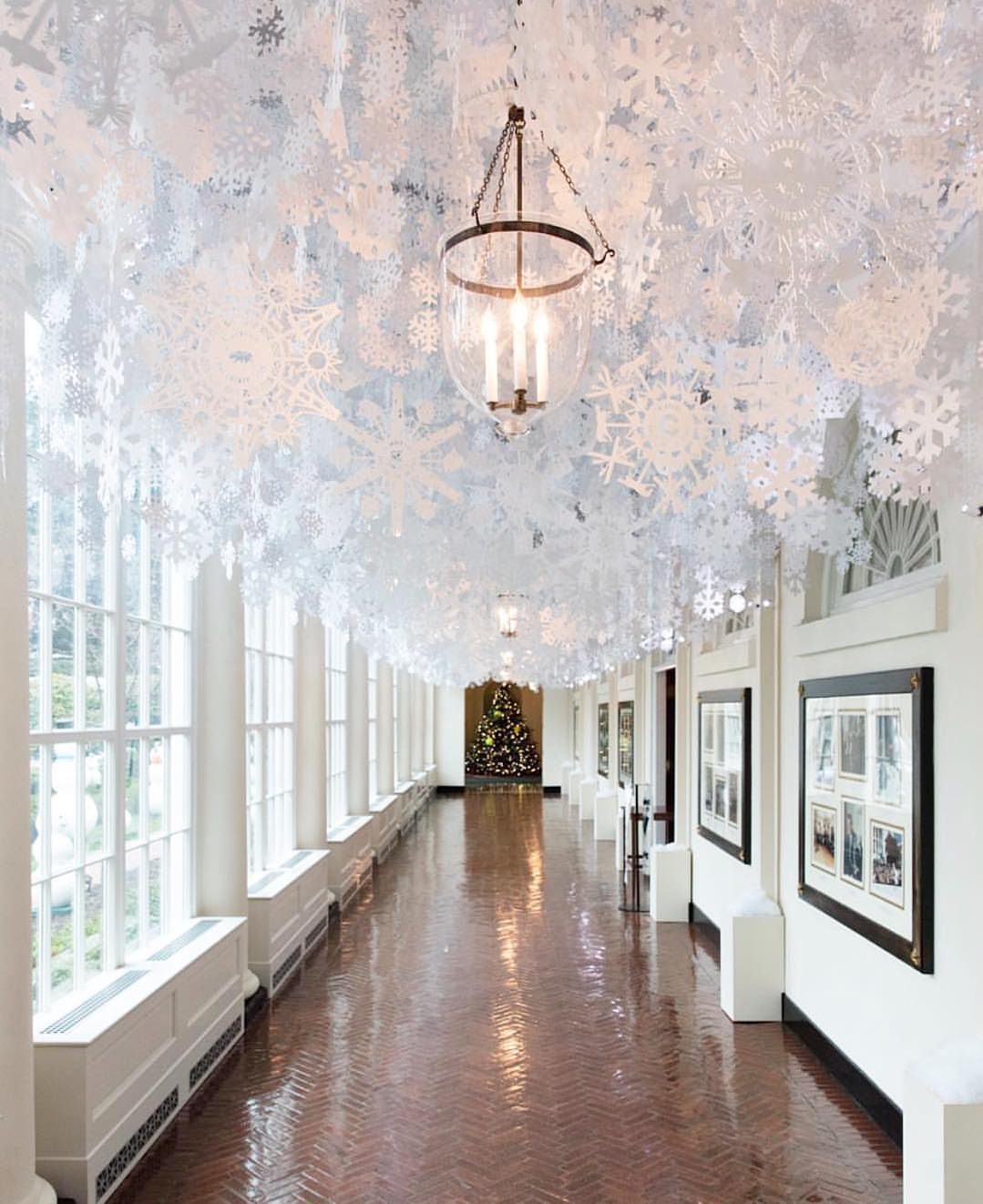 9 Ceiling Christmas Decor Ideas for 2026 8 White snowflake decorations hanging densely from the ceiling of a long, bright hallway.