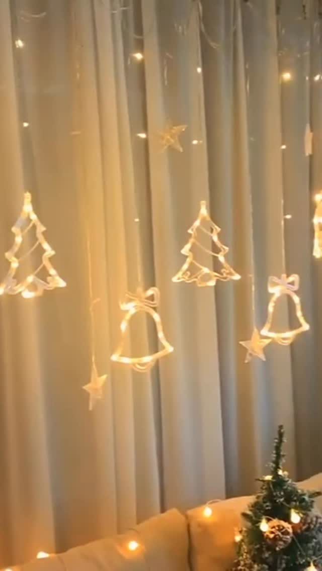 9 Ceiling Christmas Decor Ideas for 2026 2 Glowing fairy lights hanging against white curtains in shapes of trees, bells, and stars.