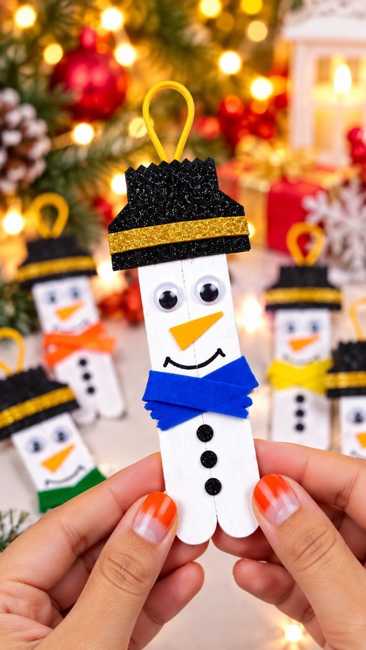 25 Christmas Art and Craft Ideas for Cards, Ornaments, and Decor 11 Hands holding a handmade popsicle stick snowman ornament with a black glitter hat and blue bow tie.