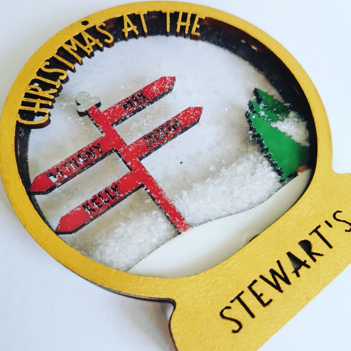 25 Christmas Art and Craft Ideas for Cards, Ornaments, and Decor 21 A gold-rimmed Christmas bauble featuring a snowy landscape with red signs and a green tree.