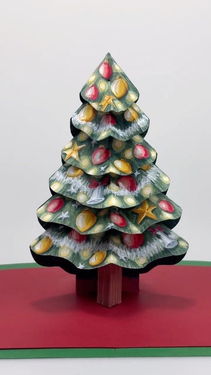 25 Christmas Art and Craft Ideas for Cards, Ornaments, and Decor 5 A decorated green pop-up Christmas tree card with colorful ornaments on a red base.