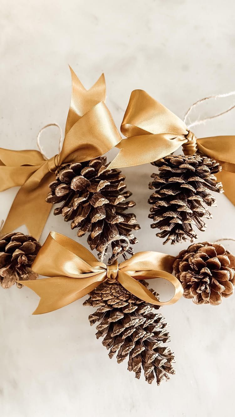 25 Christmas Art and Craft Ideas for Cards, Ornaments, and Decor 13 Glittery gold pine cones tied with large satin bows on a white background.