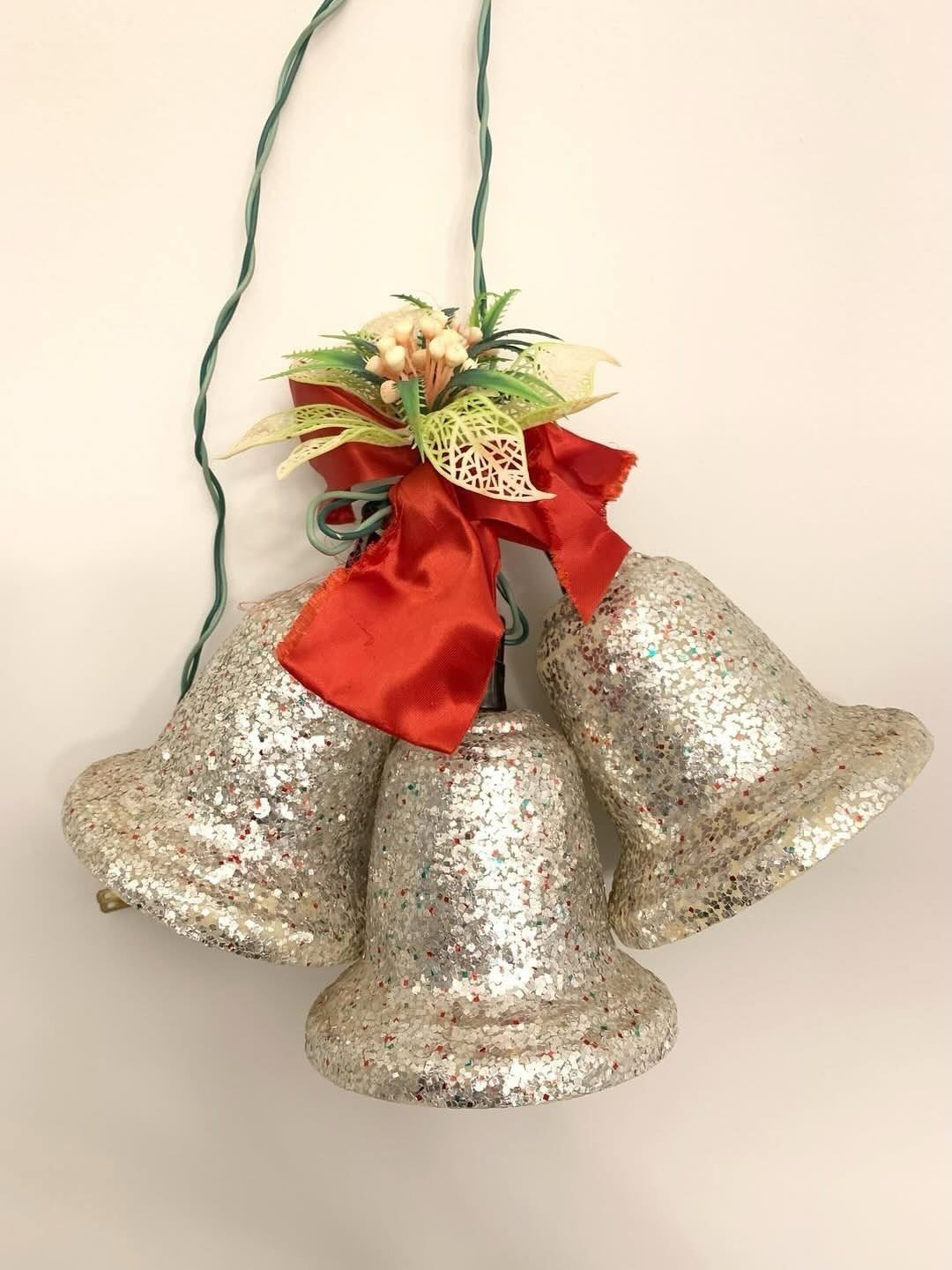 25 Christmas Art and Craft Ideas for Cards, Ornaments, and Decor 12 Three silver glitter bells decorated with a red satin bow hanging against a white wall.