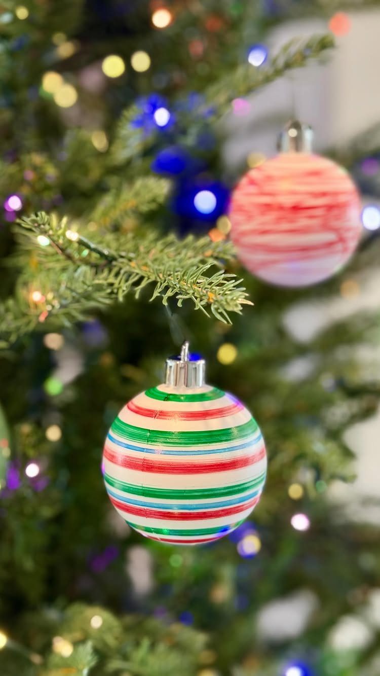 25 Christmas Art and Craft Ideas for Cards, Ornaments, and Decor 9 Striped round Christmas ornaments hanging on a glowing, decorated evergreen tree.