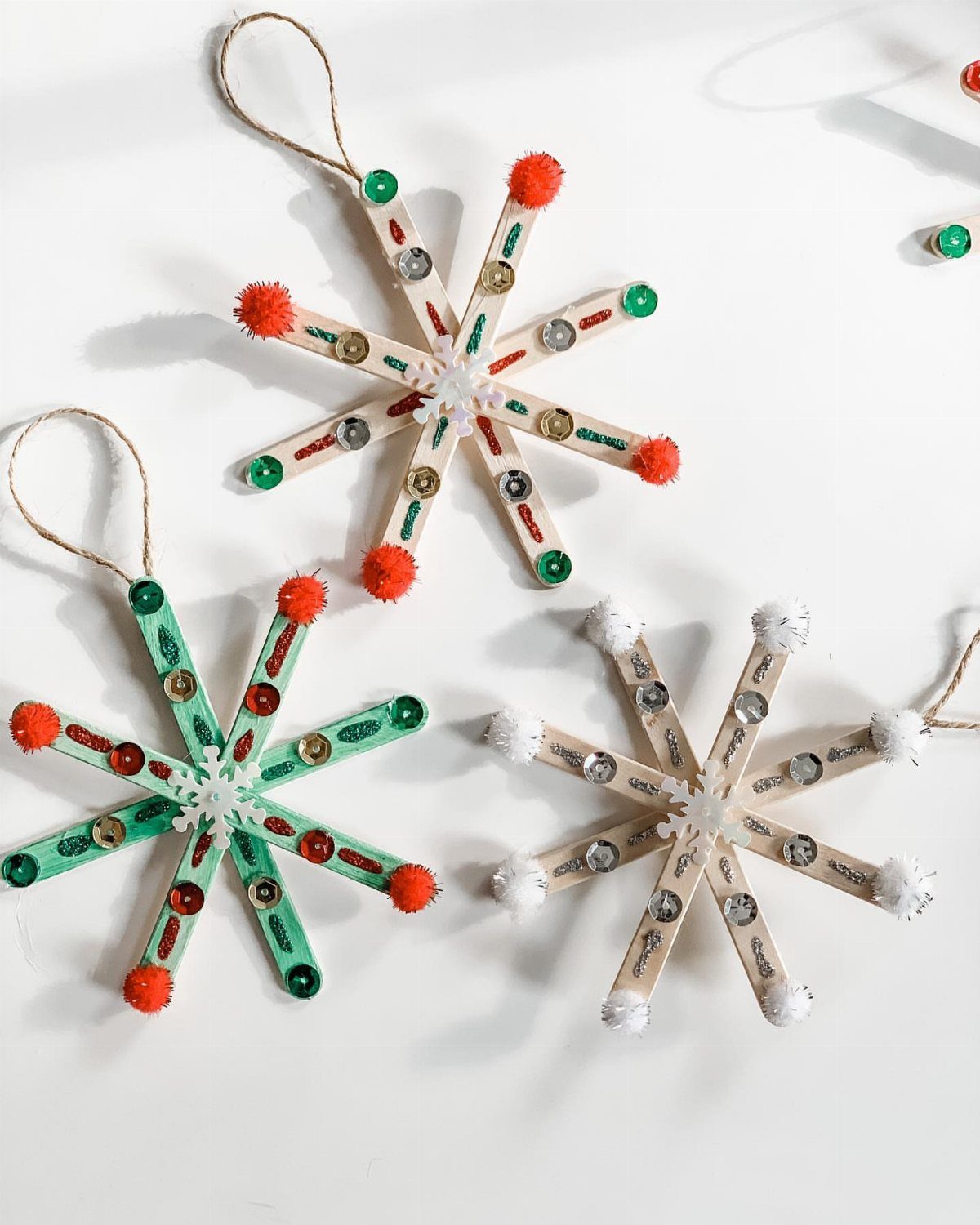 25 Christmas Art and Craft Ideas for Cards, Ornaments, and Decor 3 Three colorful snowflake ornaments crafted from decorated popsicle sticks on a white background.