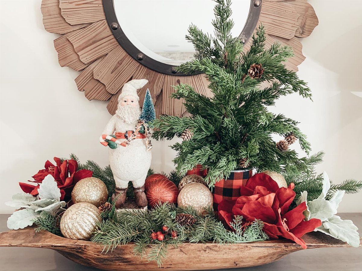 Christmas Decorations with Pinecones: 17 Ideas for Your Home 15 Wooden dough bowl filled with Christmas greenery, red flowers, gold ornaments, and a small Santa figurine.