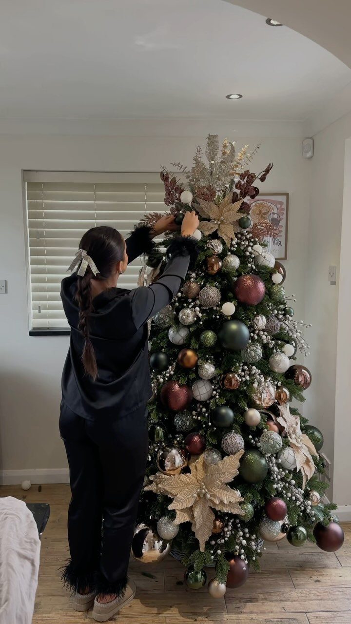 Christmas Decorations with Pinecones: 17 Ideas for Your Home 5 A person decorating a large Christmas tree with gold, red, and green ornaments.