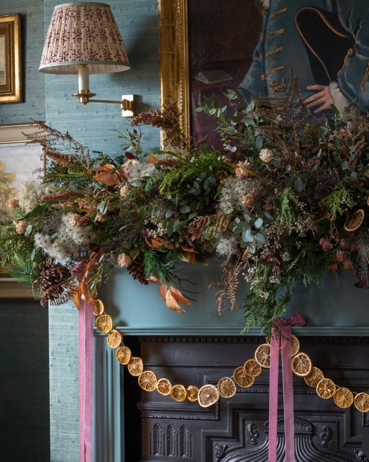 Christmas Decorations with Pinecones: 17 Ideas for Your Home 7 Greenery, dried flowers, and pinecones arranged on a teal mantelpiece with citrus garland.