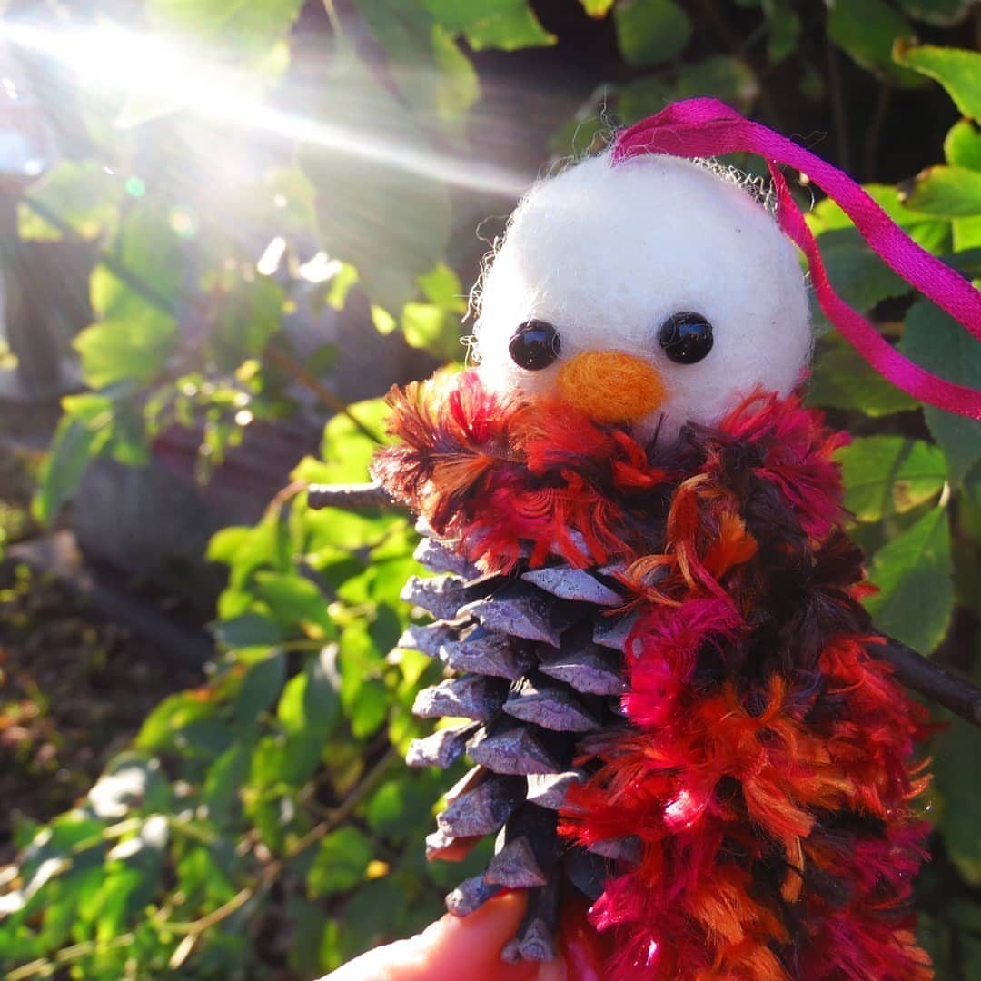 Christmas Decorations with Pinecones: 17 Ideas for Your Home 3 Handmade pinecone snowman ornament with a white felt head and colorful feathered body held outdoors.
