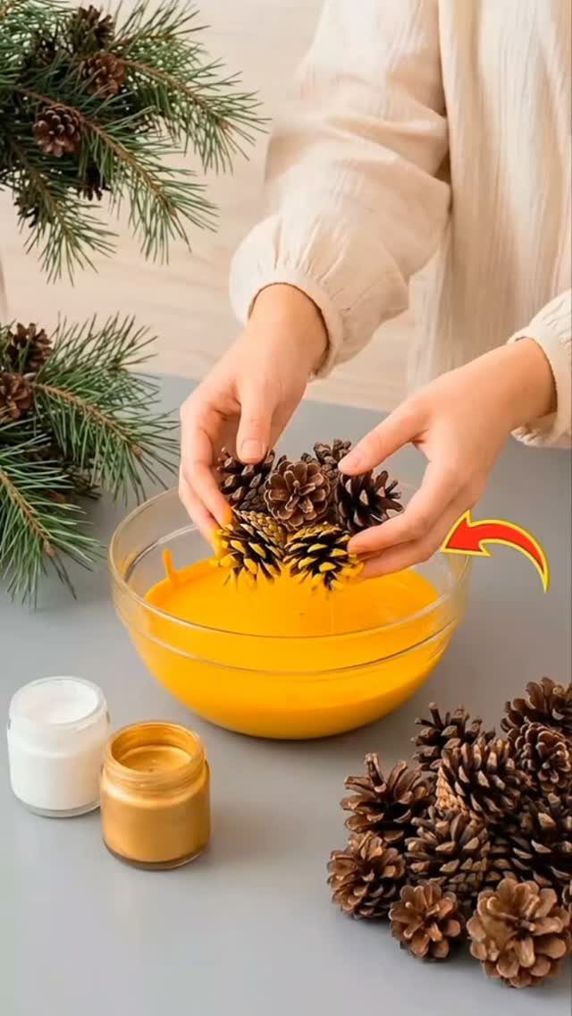 Christmas Decorations with Pinecones: 17 Ideas for Your Home 8 Hands dipping pinecones into a bowl of yellow paint on a grey tabletop.