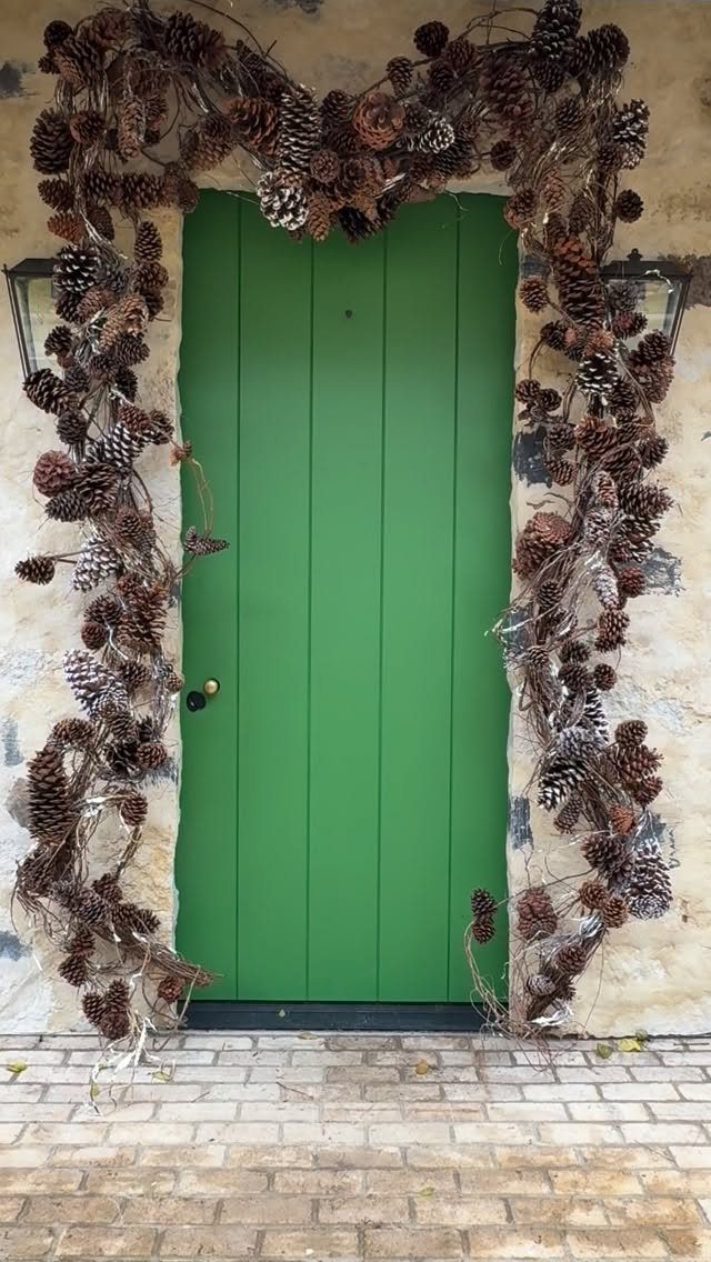 Christmas Decorations with Pinecones: 17 Ideas for Your Home 4 A large pinecone garland draped around a bright green wooden door.