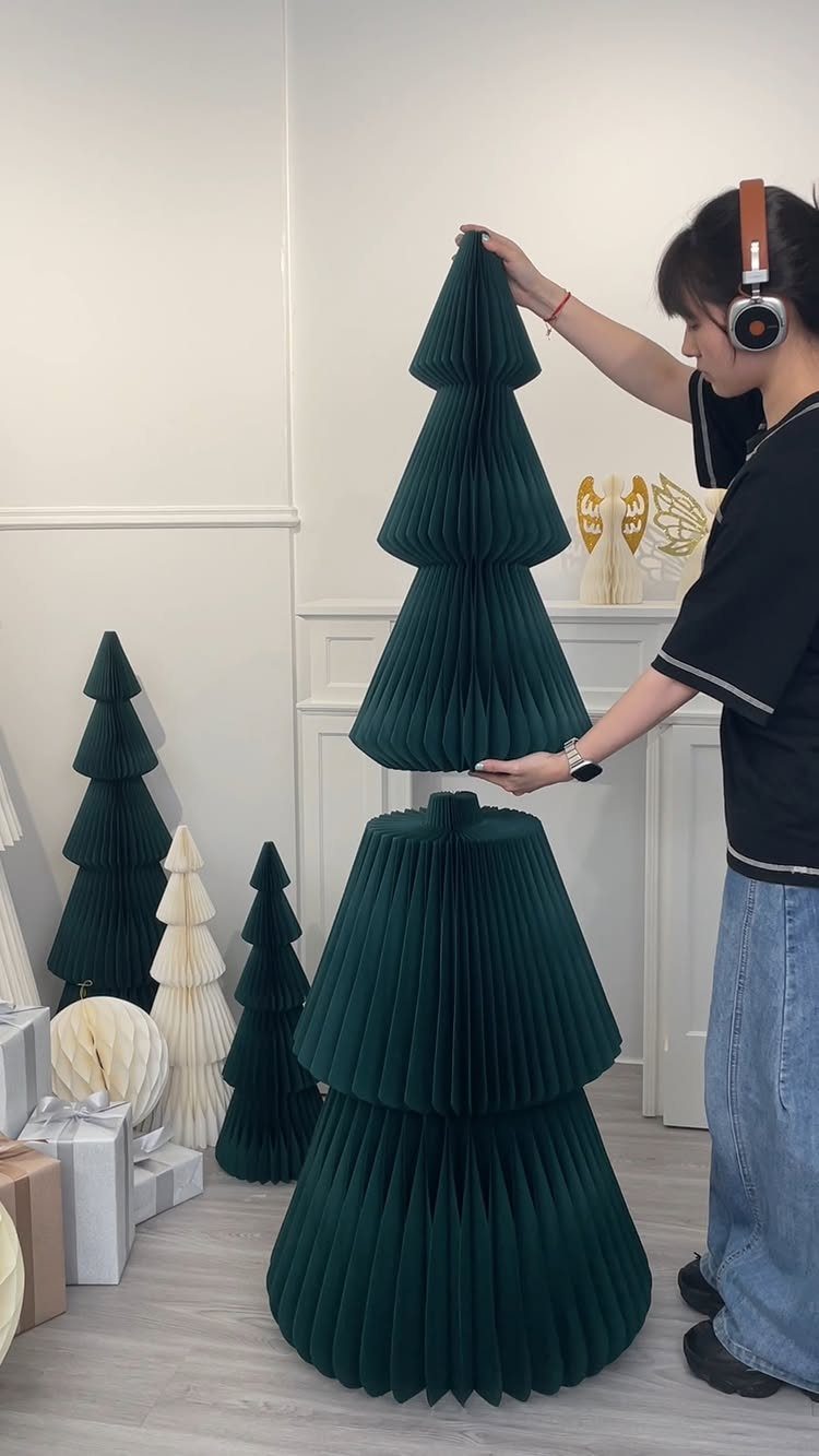 5 Christmas Stairs Decor Ideas: Garland, Bells, Paper Orbs & More 5 A person holding a large dark green honeycomb paper tree among several other paper trees.
