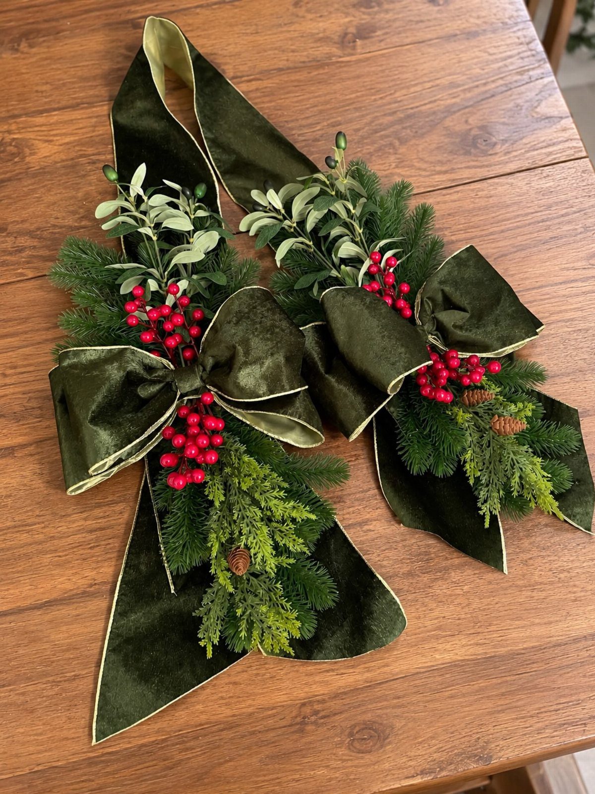 5 Christmas Stairs Decor Ideas: Garland, Bells, Paper Orbs & More 3 Two green velvet bows with red berries and evergreen sprigs on a wooden table.