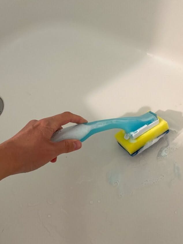 Cleaning Checklist by Room: 4 Lists That Actually Get Finished 3 A hand using a blue and yellow sponge to scrub soapy foam in a white bathtub.
