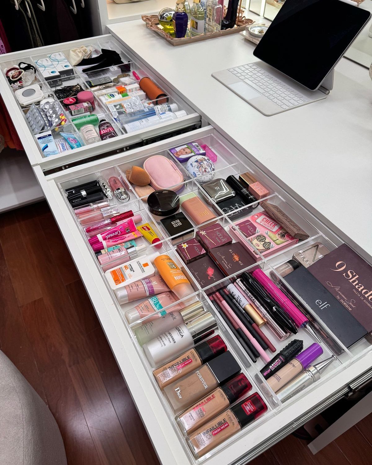 Makeup products organized in clear acrylic dividers within an open white vanity drawer.