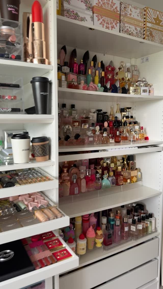 Perfume bottles and makeup products arranged on white shelves in a organized collection.