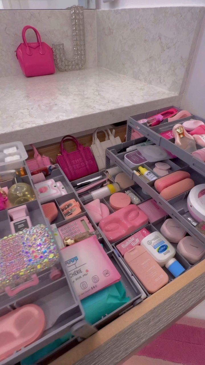 Open drawer containing various pink makeup and skincare products organized in grey plastic dividers.