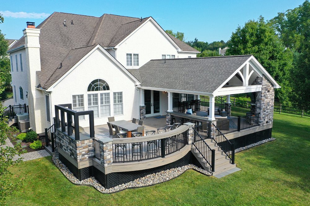 6 Covered Patio Grill Area Ideas for Any Yard 2 An elevated wooden deck with a dining area and a covered pavilion attached to a white house.